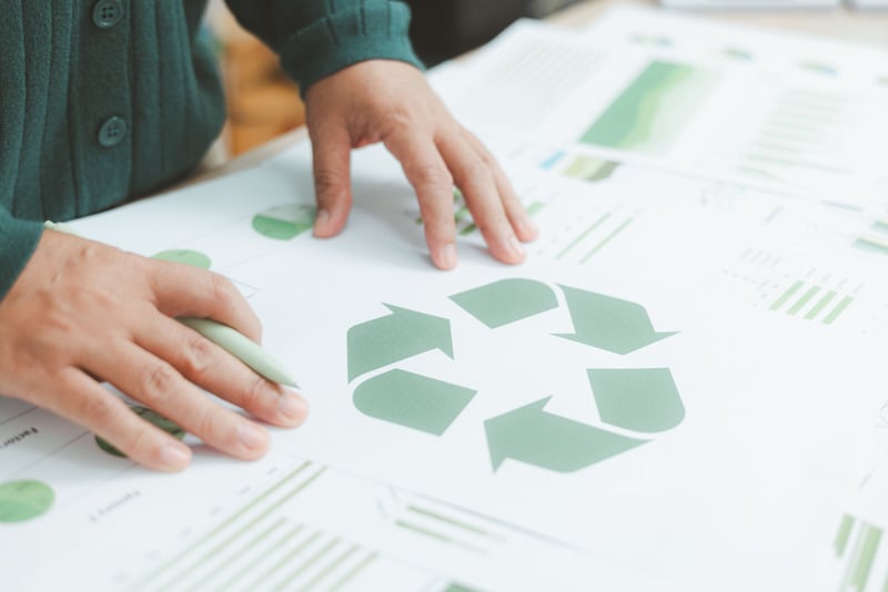 Hands tracing a green recycling symbol on printed reports with charts nearby.